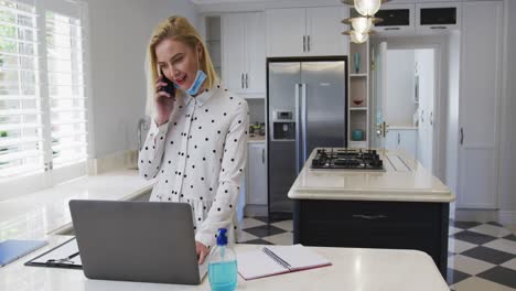 woman talking on smartphone while using laptop in the kitchen