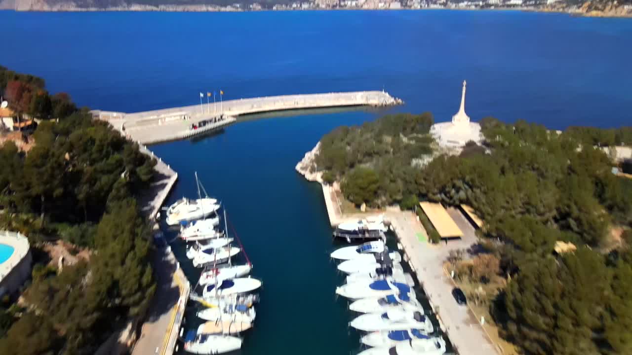 Enjoy a stunning view of the marina in Santa Ponsa, Mallorca, showcasing various luxury boats lined up by the calm turquoise waters under a bright sun.