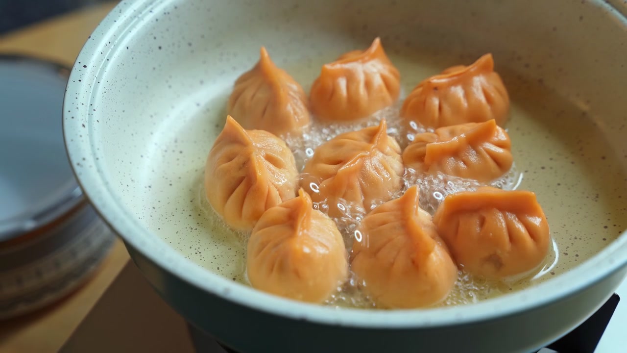 Pengambilan gambar close-up tutup kaca yang menutup panci berisi pangsit oranye mendidih. Dim sum Asia segar dimasak dalam cairan mendidih di dapur modern dalam ruangan.