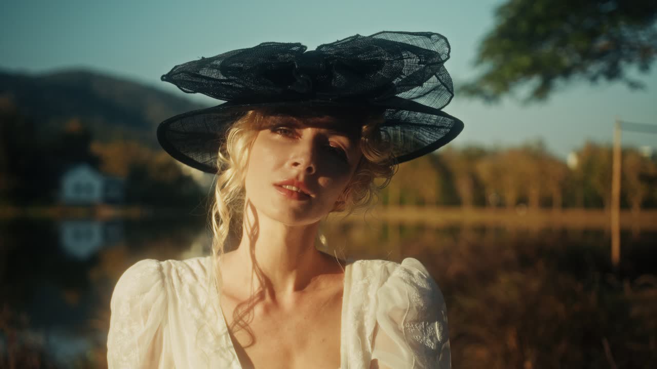 Elegant Woman in Vintage Dress and Hat Posing by a Lake at Golden Hour