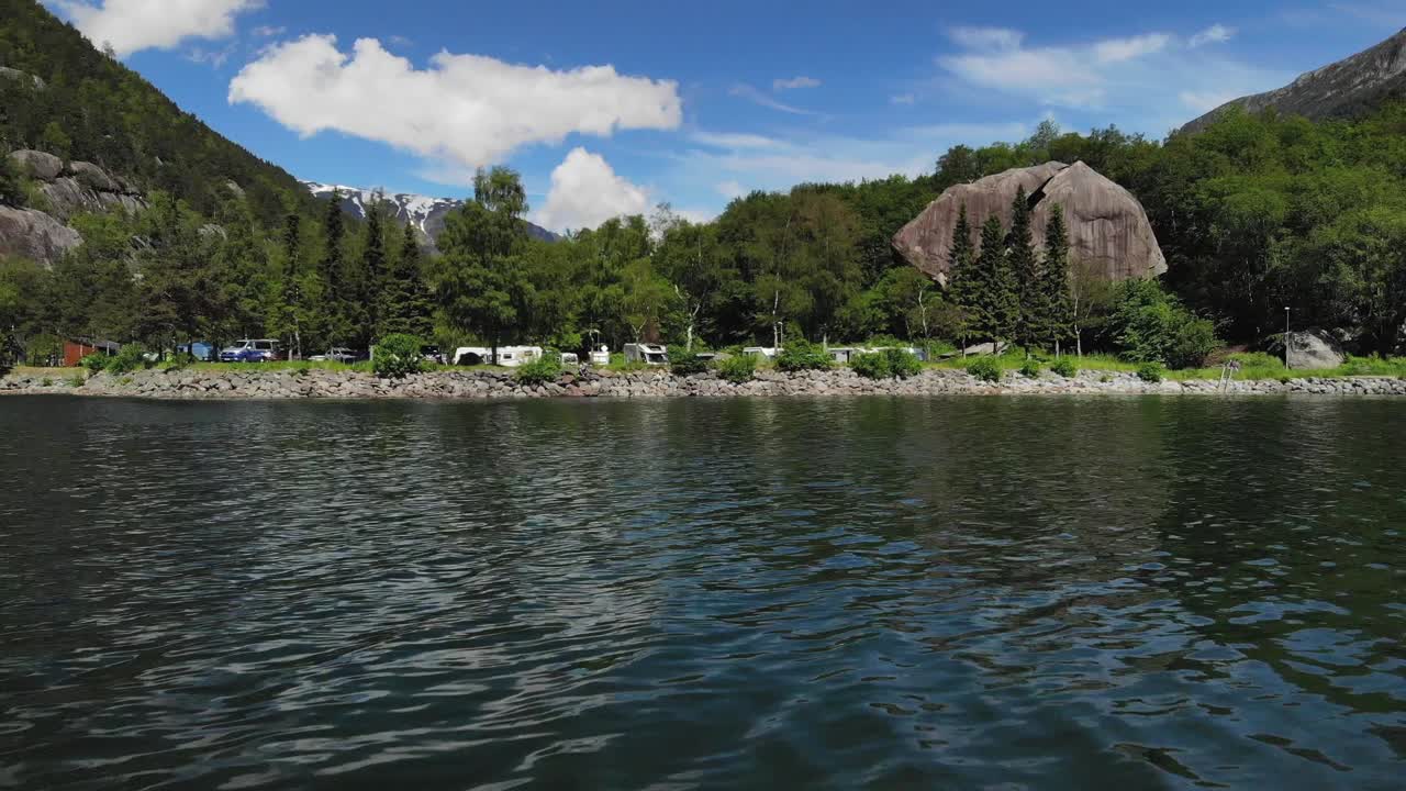 дрон летит близко к воде в направлении парковки, заполненной автофургонами