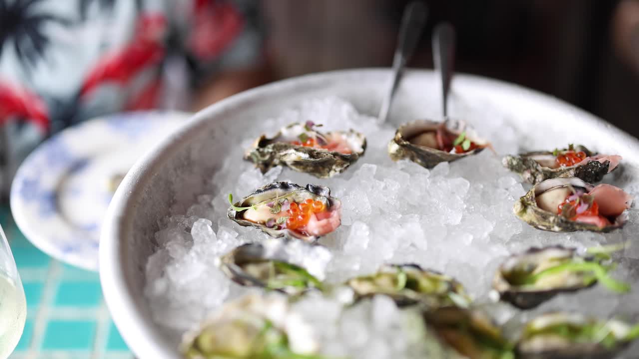 Hands garnishing oysters with toppings on ice