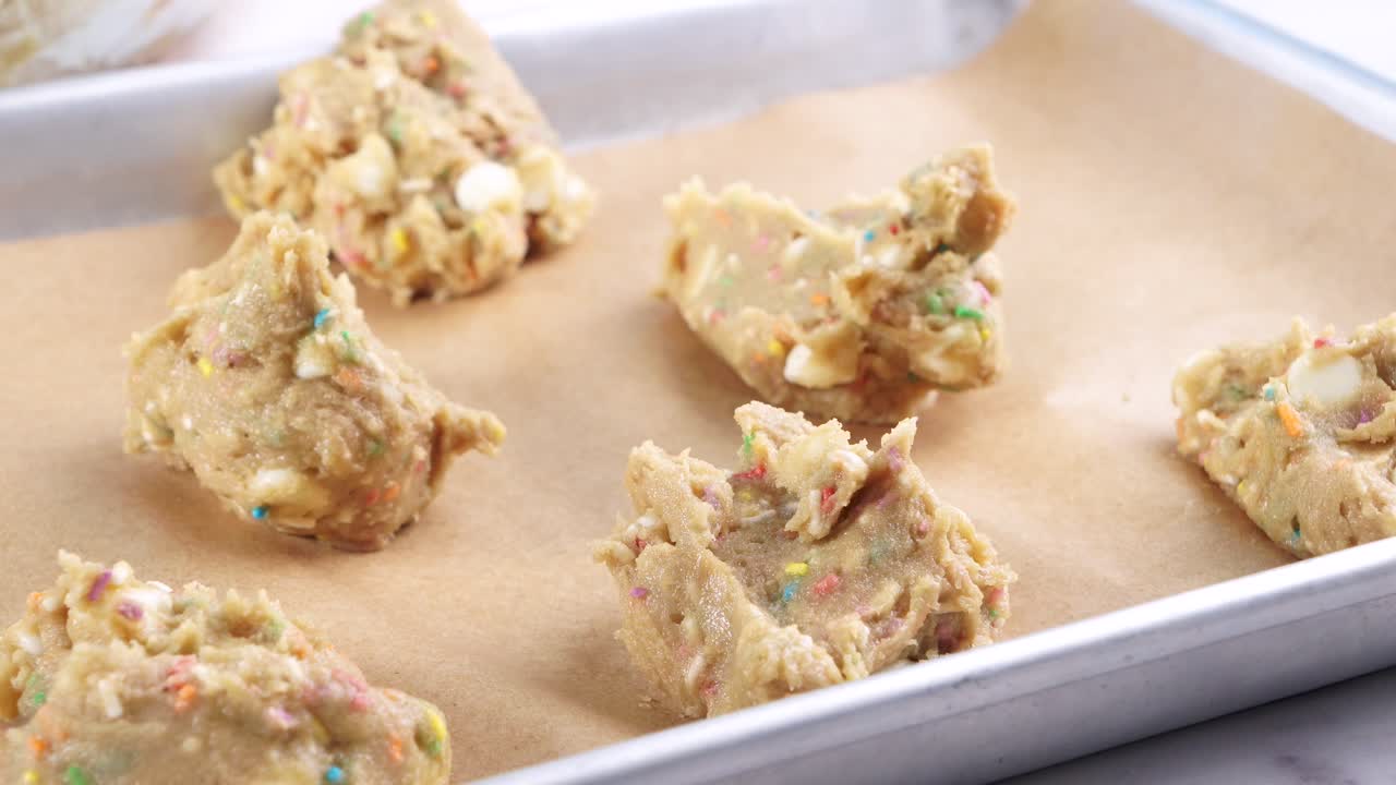Baking confetti sugar cookies and placing them on a baking sheet. Making cookies and placing the batter on a sheet with a spoon to bake.. In the kitchen making a dessert