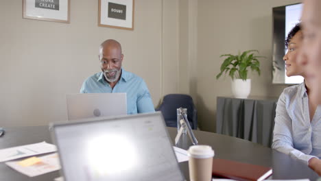 Diverse-business-people-using-laptops-at-conference-table-with-copy-space