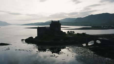 drone shot approaching the silhouette of a castle on an island in scotland's countryside