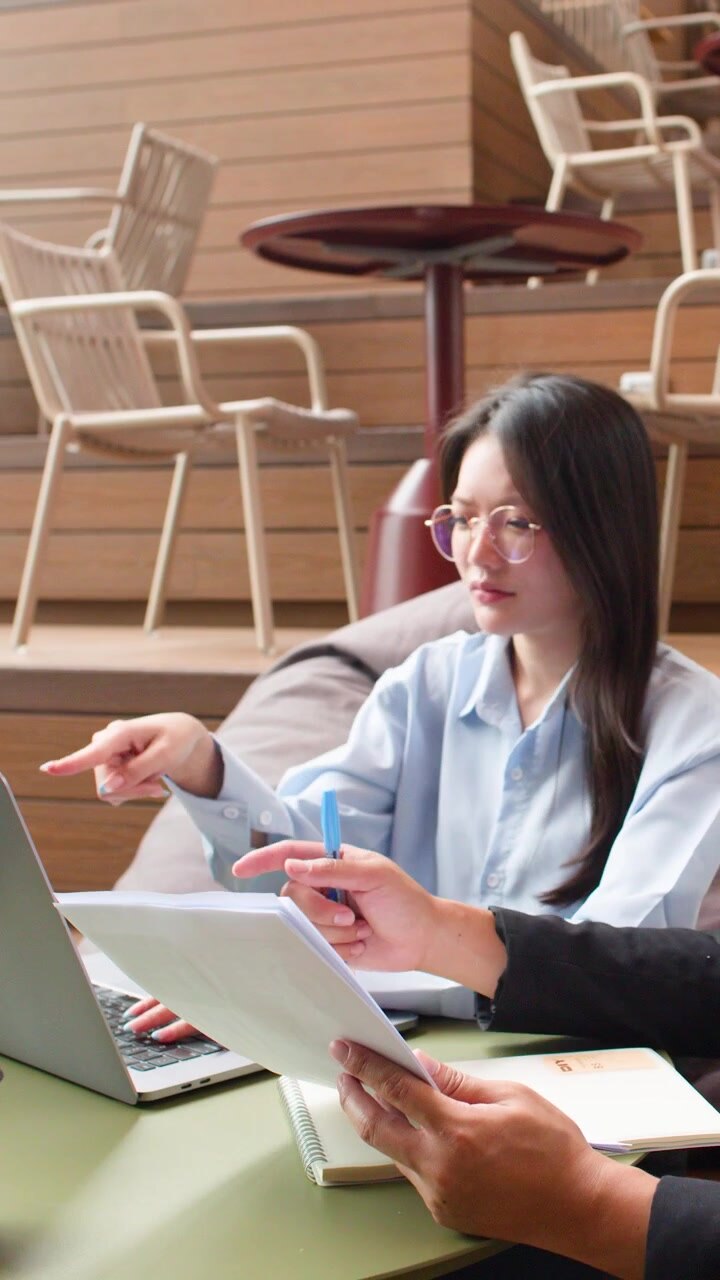 Imprenditrice asiatica con occhiali collabora su documenti con un collega in un moderno spazio di coworking