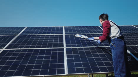 vista trasera del hombre lavando paneles solares en la planta de energía doméstica