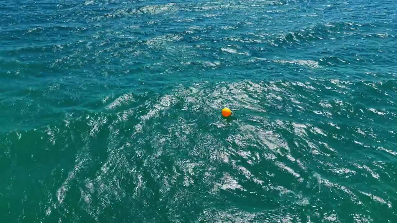 Waves move around a bright orange buoy floating in the blue sea during a sunny day