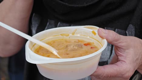 woman eating cabbage soup with lots of meat and a slice of bread from a plastic bowl. outside. event