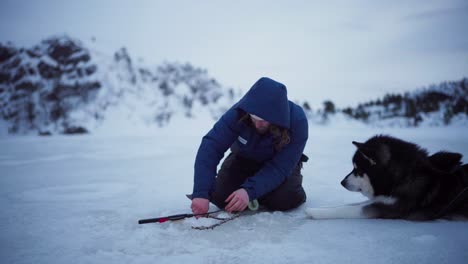 Un-Hombre-Acompañado-Por-Su-Perro-Capturó-Con-éxito-Un-Pez-Mientras-Pescaba-En-El-Hielo-En-Bessaker,-Condado-De-Trondelag,-Noruega---Toma-Estática