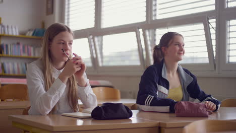 two female pupils raising hands to answer the question in a classroom, handheld