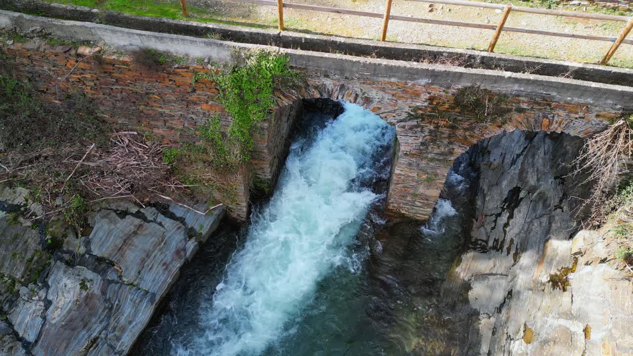 Imagem de drone de um rio caudaloso passando por baixo de uma ponte histórica de pedra na Extremadura, Espanha, cercado por paisagem rochosa e cenário natural. Um pitoresco marco de viagem europeu.