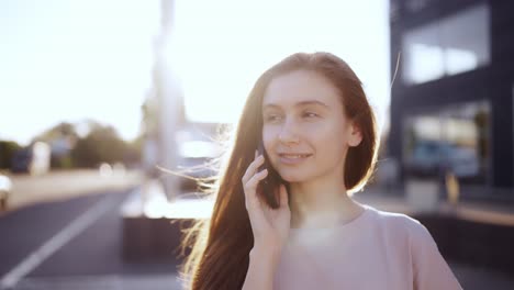 Mujer-Feliz-Hablando-Por-Teléfono-Móvil-Al-Aire-Libre,-Destellos-De-Lente-En-El-Fondo,-Cámara-Lenta