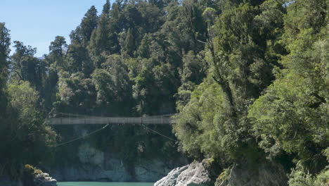 slow motion pan down over a bridge across a turquoise blue river - hokitika gorge, new zealand