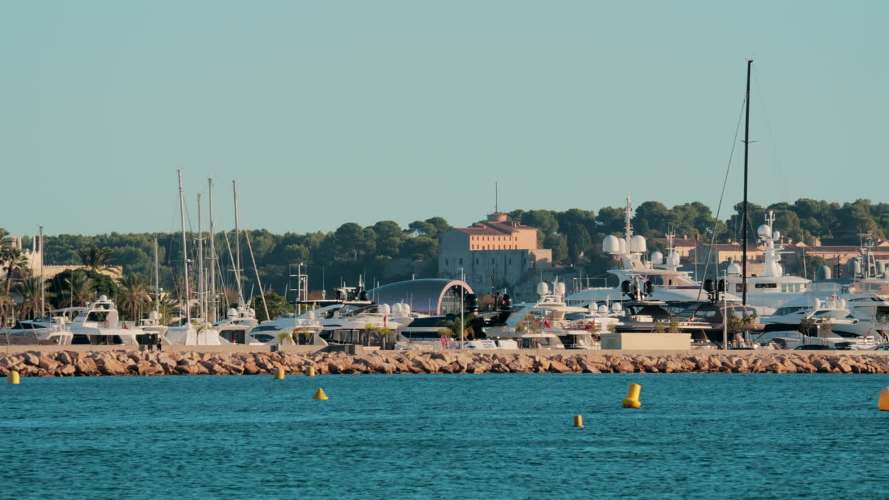 Dozens of luxury yachts anchored in thePort Pierre Canto in Cannes, with scenic coastal architecture and calm blue sea