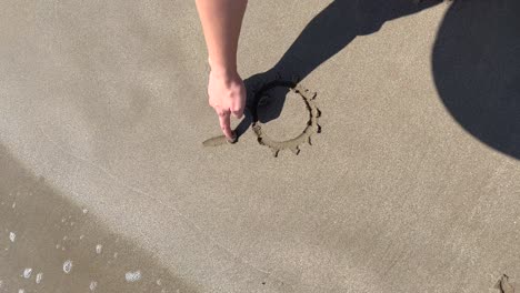 Frau-Zeichnet-Eine-Sonne-Im-Sand-Am-Strand,-Vertikale-Ansicht