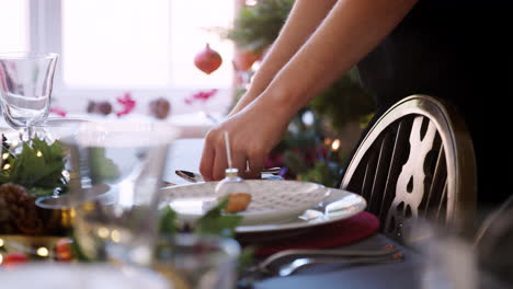 Primer-Plano-De-Las-Manos-De-Una-Mujer-Poniendo-Cubiertos-De-Plata-En-Una-Mesa-De-Comedor-Decorada-Para-La-Cena-De-Navidad,-Enfoque-Selectivo