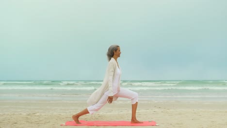 vista lateral de una mujer afroamericana senior activa haciendo ejercicio en una alfombra de ejercicio en la playa 4k