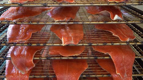 overview of recently smoked rainbow trout fillets resting on grillage - lower tray beeing pulled out by worker