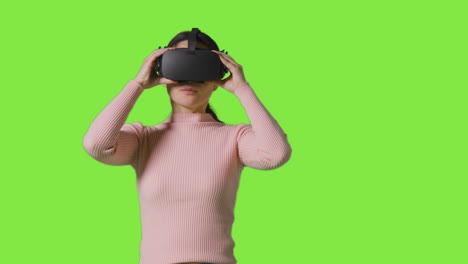 woman putting on virtual reality headset against green screen studio background