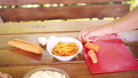 Close-up-Guy-is-cooking-pilaf-He-is-in-a-summer-house-cuts-carrots-on-a-red-cutting-board-Preparing-for-a-picnic