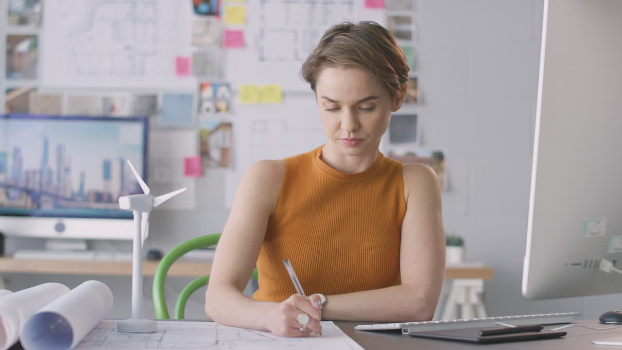 arquitecta femenina en la oficina trabajando en dibujos para un proyecto de energía renovable con un modelo de turbina eólica
