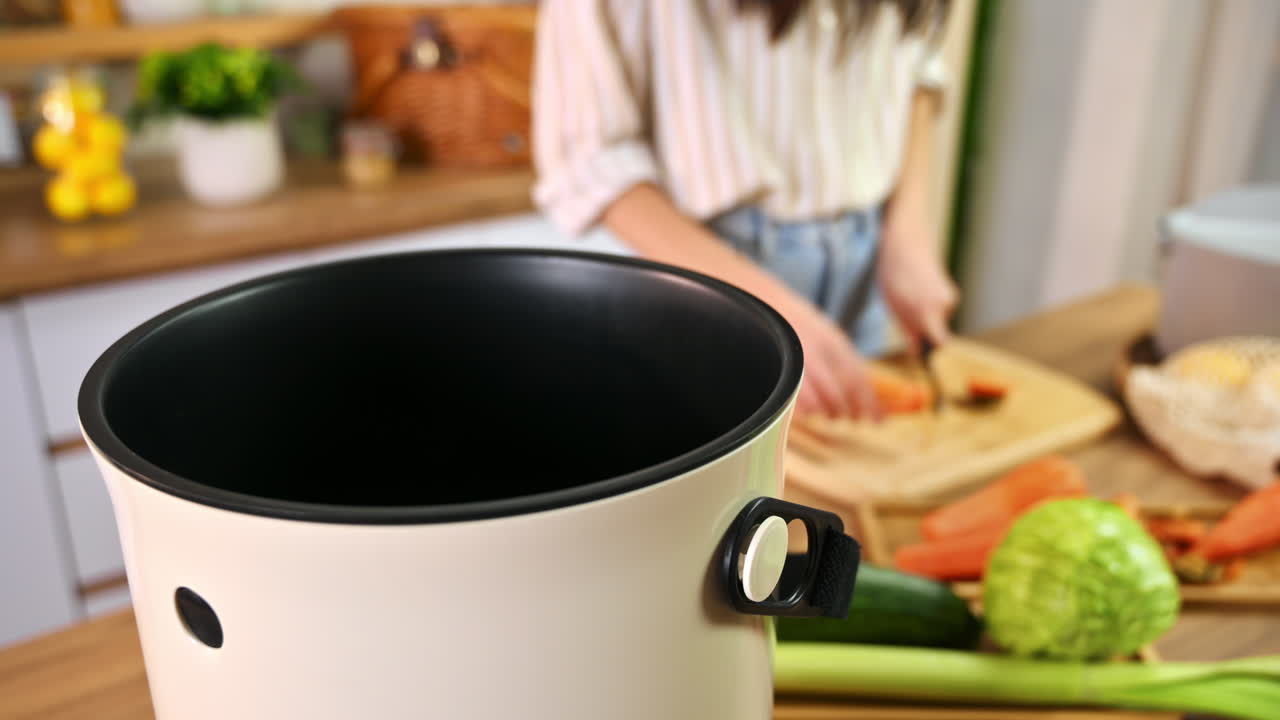 Young woman recycling vegetables peels in a compost bin. Housewife cooking food and composting organic waste in a bokashi container at home. Ecological and sustainability concept