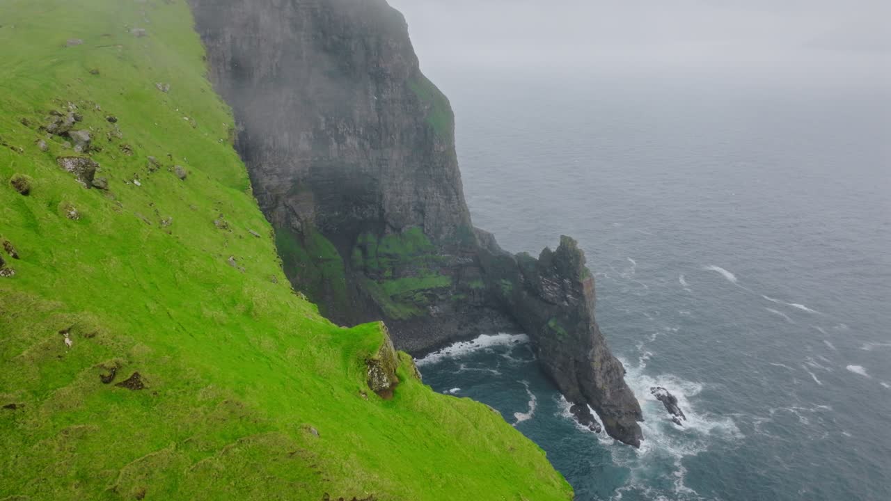 Misty faroe cliffs, green grass, and waves crashing below, serene mood, aerial view, Kallur Lighthouse