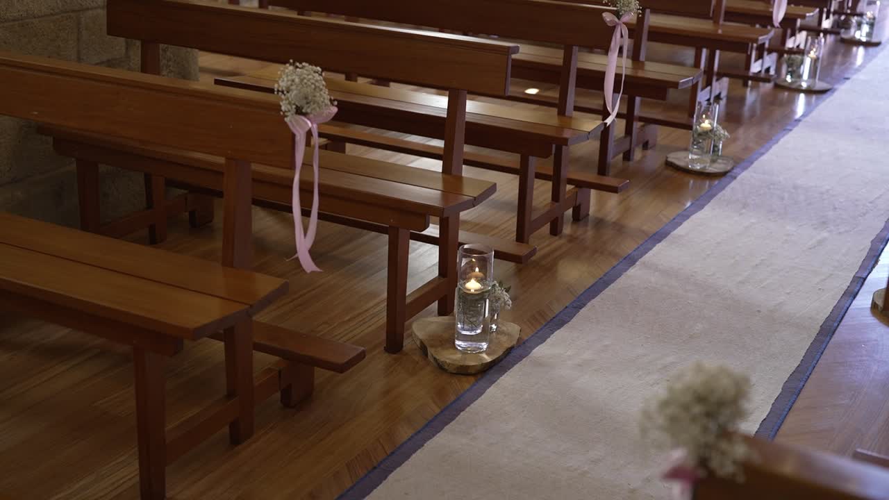 pasillo de bodas con bancos de madera, decoraciones florales y jarrones a la luz de velas en un entorno de iglesia