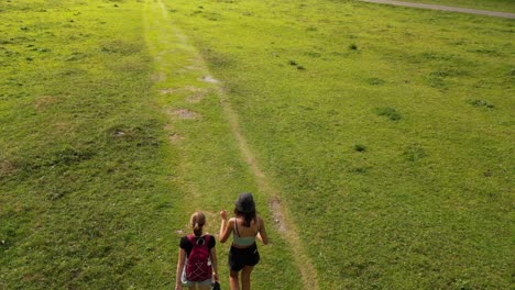 two girls talk and walk on a small gravel path on a green meadow in the swiss alps, obwalden, drone alp view