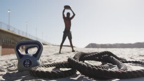 African-american-man-lifting-ball-exercising-outdoors-on-beach