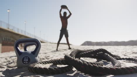 hombre afroamericano levantando la pelota haciendo ejercicio al aire libre en la playa