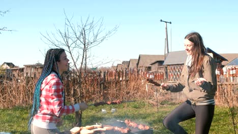 two women friends cook shashlik meat on top of charcoal grill on backyard. talking and smiling together, have a rest in weekend.