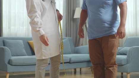 médico masculino asiático con un paciente masculino gordo en la clínica. el paciente midiendo el peso usando una balanza, el médico usando cinta midiendo la cintura del paciente