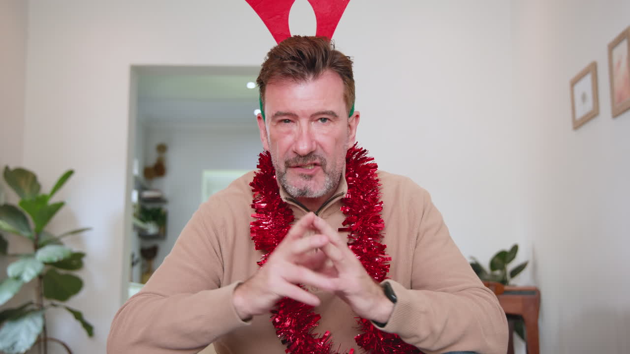 Senior man wearing reindeer antlers and tinsel, celebrating Christmas at home