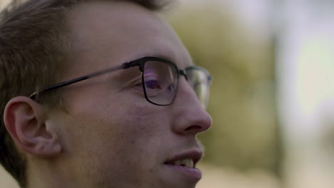 young man in eyeglasses laughing and talking to someone outdoor