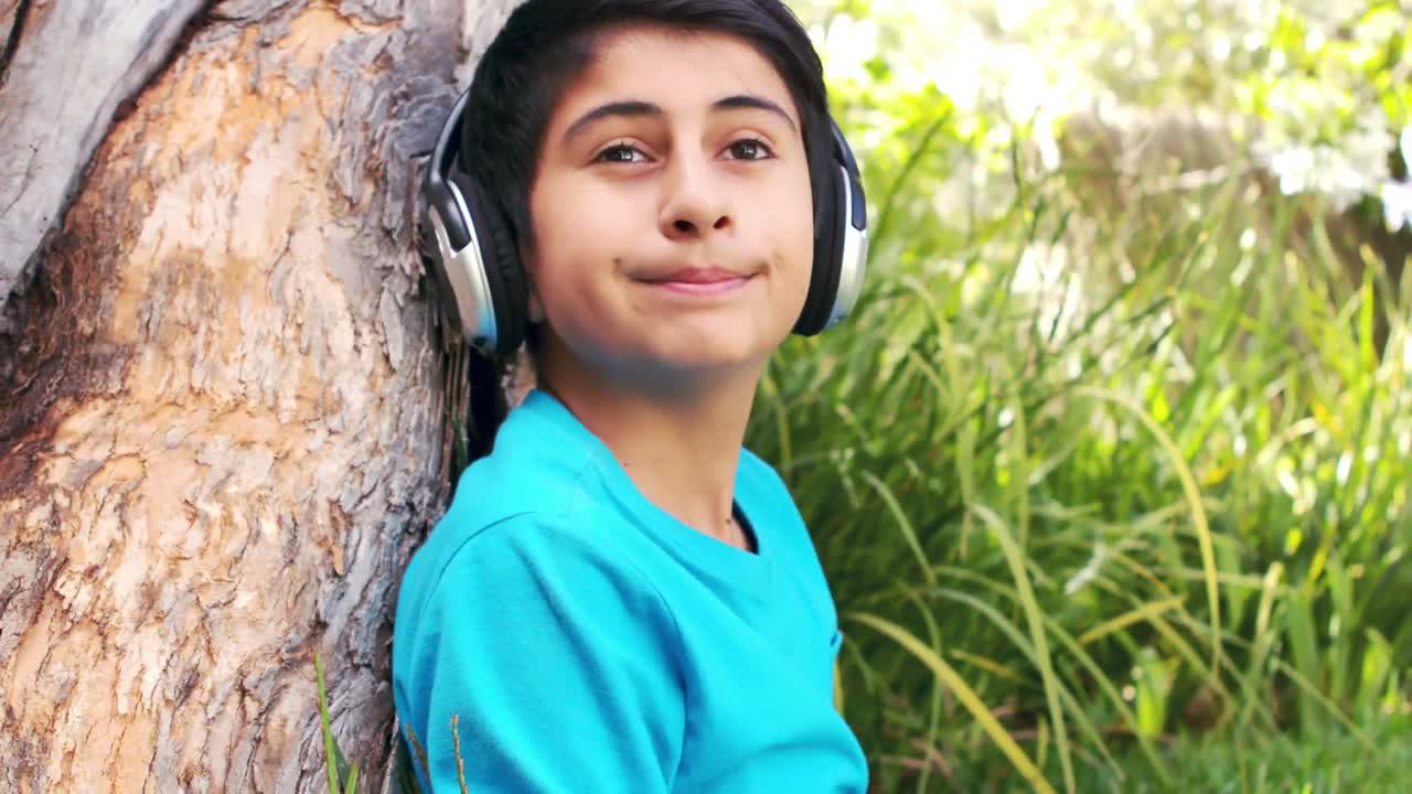 niño lindo escuchando música con auriculares sentado en la hierba