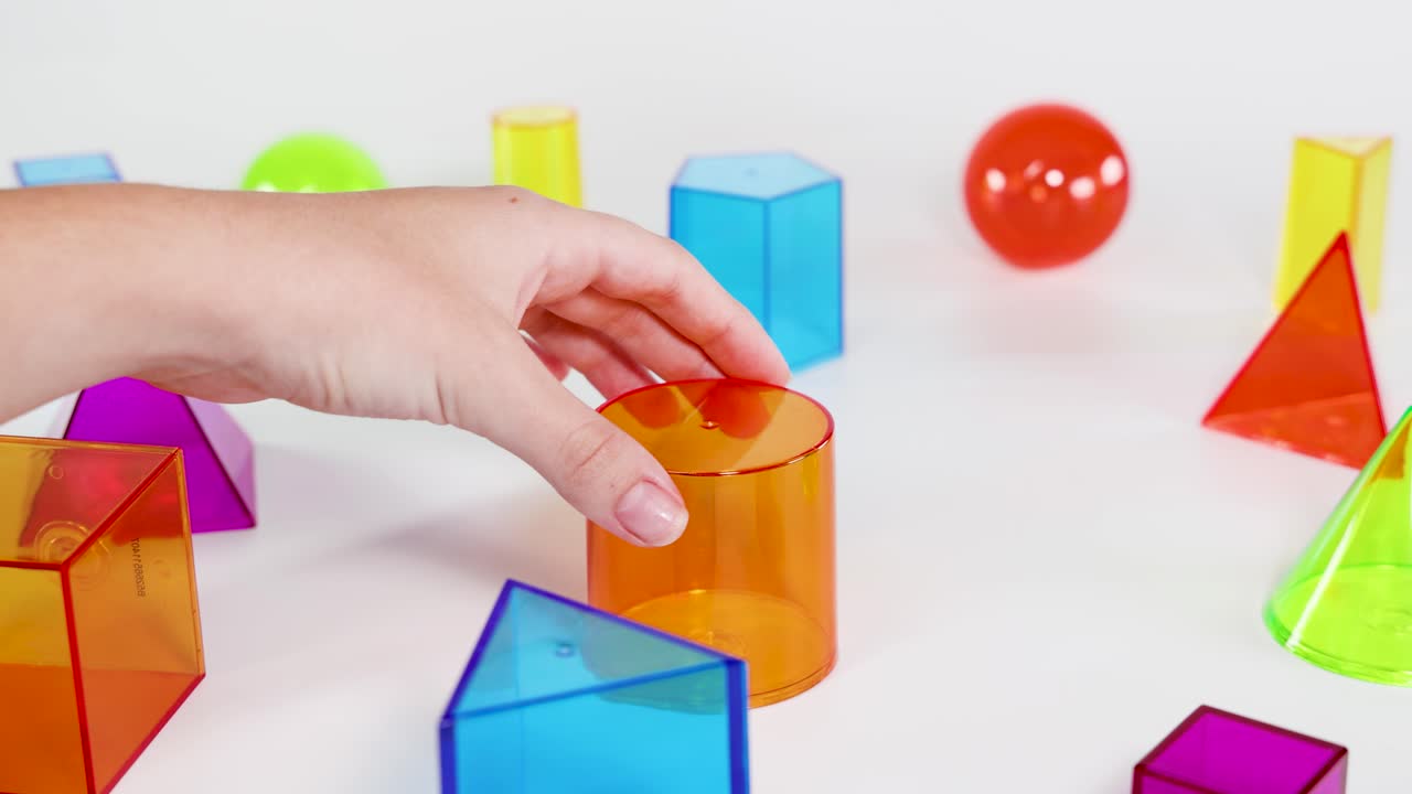 Hands stack colorful 3D geometric shapes on a table, demonstrating balance and coordination in a well-lit environment