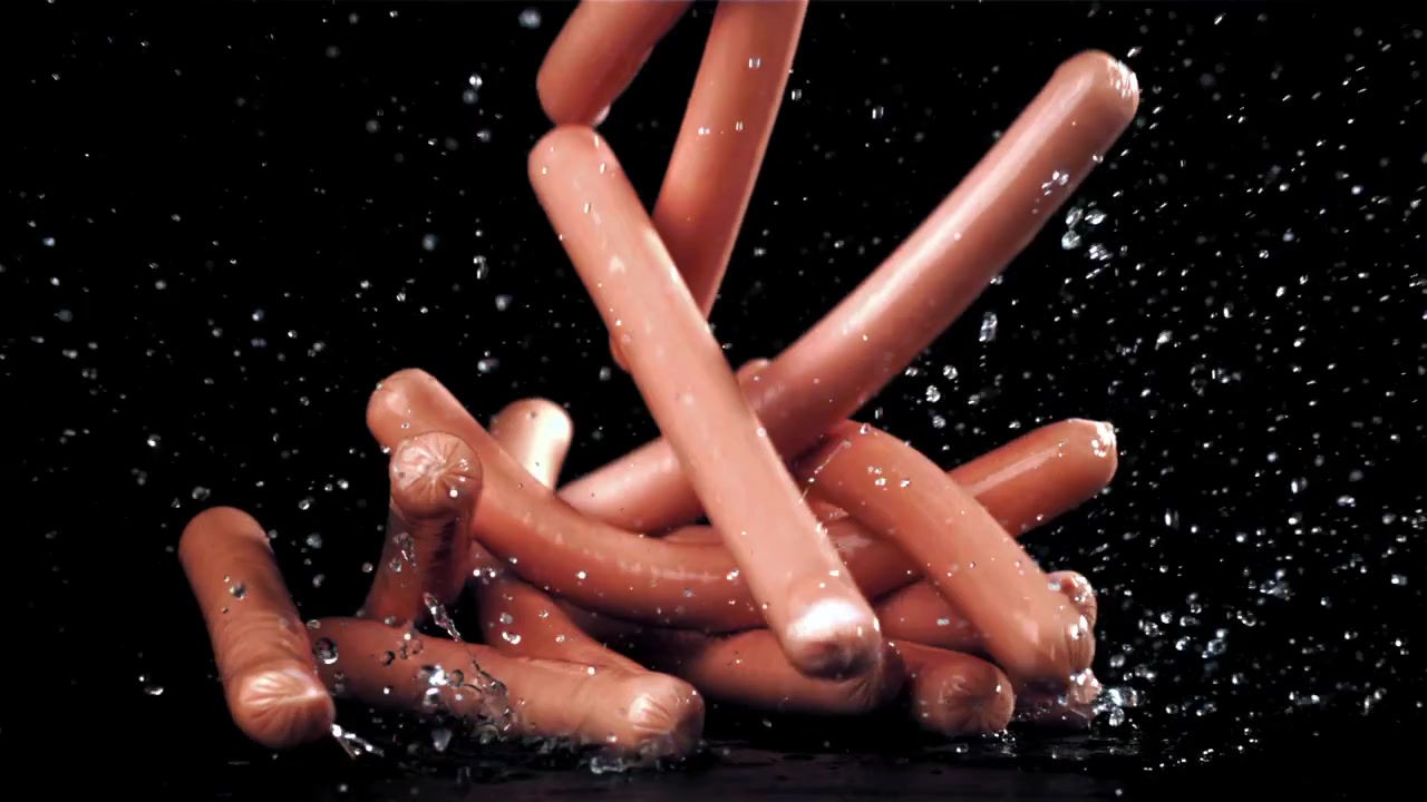 Salsicce crude che cadono su una superficie bagnata al rallentatore.