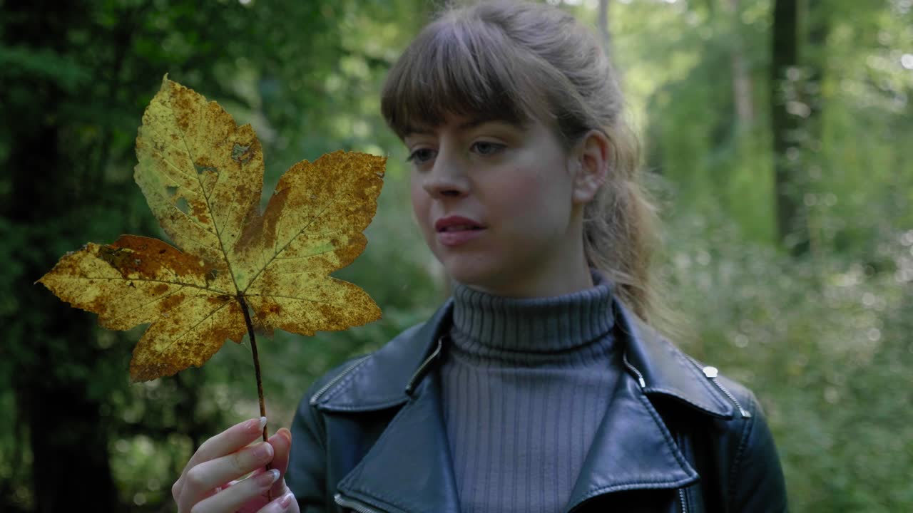 Young woman examining an autumn leaf in the forest