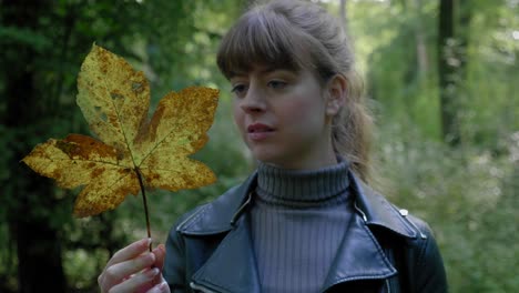young woman examining an autumn leaf in the forest