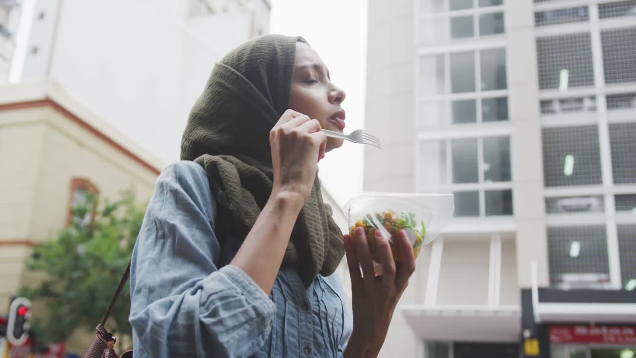 mujer con hijab comiendo una ensalada para llevar en la calle
