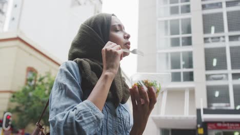 Woman-wearing-hijab-eating-a-takeaway-salad-in-the-street-