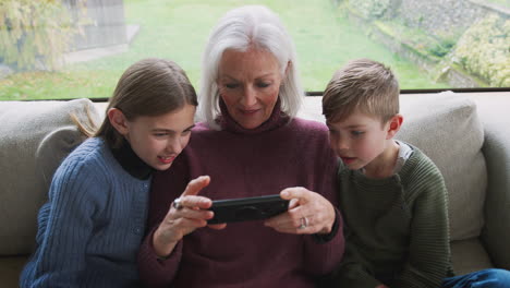 abuela jugando videojuegos con los nietos en el teléfono móvil en casa