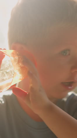 curious little boy puts empty glass to ear and listens sea sounds having fun in room lit by sunlight at home extreme closeup slow motion