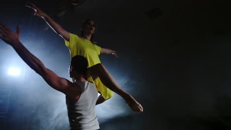 a young man is holding a woman in yellow dress and twirling in slow motion on stage in smoke and spotlights. camera is moving around a couple in medium shot