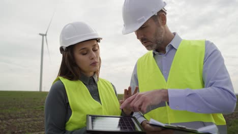 Two-caucasian-engineers-talking-together-on-wind-turbine-field.