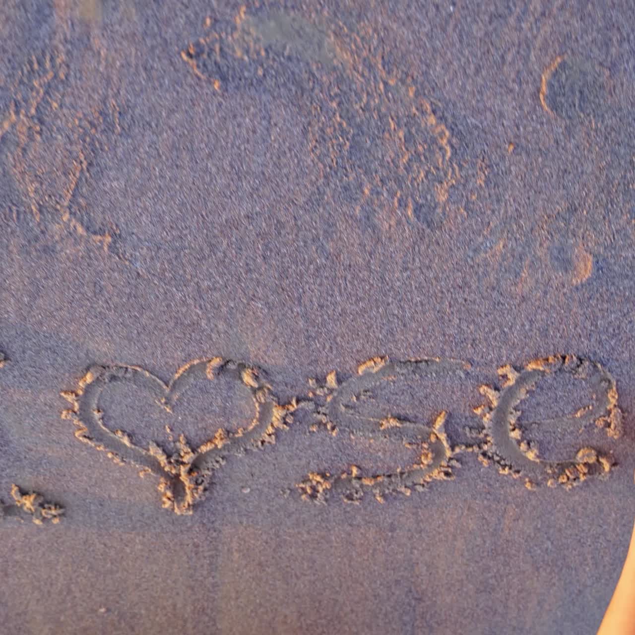 Girl painting on the sea sand. Young female is writing on a sandy beach in the evening. Top view. Close-up.