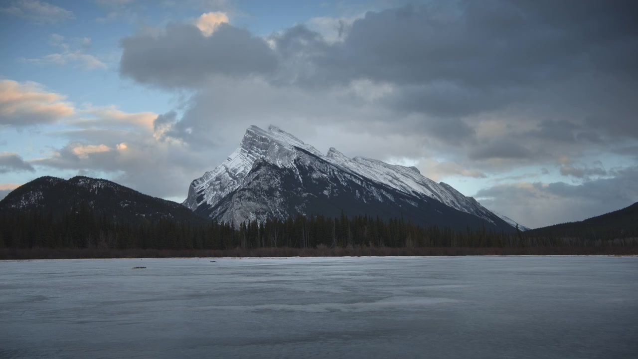 Nuvole in movimento sopra un lago ghiacciato al tramonto. Monte Rundle, Banff. Time-lapse