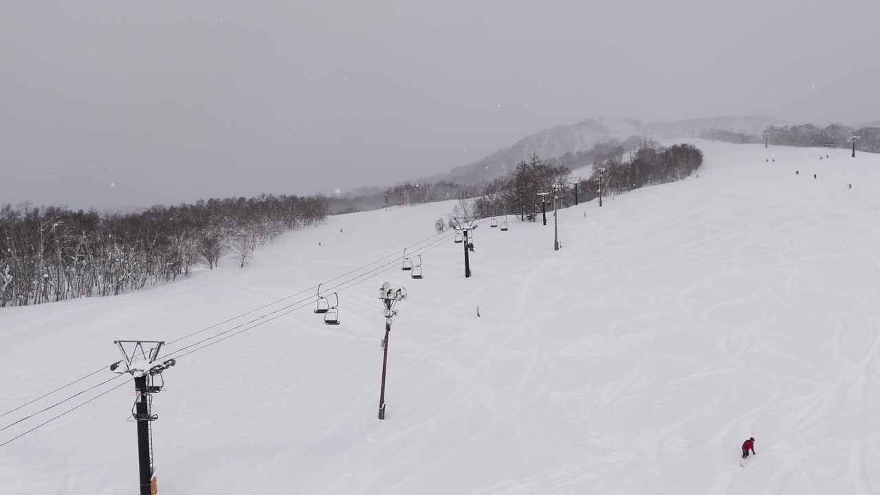 Timelapse stationary shot of an open air chair lift carrying passengers to the top of a ski slope.